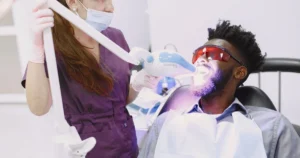 Patient wearing protective glasses during in-office teeth whitening with an LED light held by a dental professional